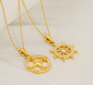 Macro shot of gold compass and helm pendants with zircon inlay on a white fabric background