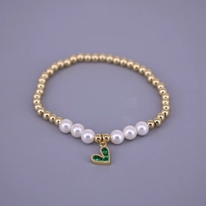 Close-up of pearl beaded bracelet featuring a gold heart charm with green zircon stones