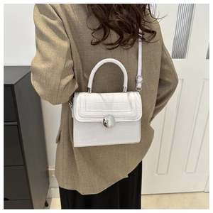 Detail of white crocodile pattern shoulder bag with silver round lock and metal hardware