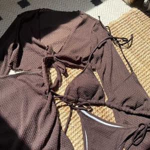 Dettaglio del bikini marrone scuro in maglia waffle con copricostume a rete su stuoia di paglia