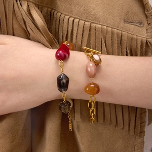 Detail of colorful resin beaded bracelets with gold chains and toggle clasp on wrist