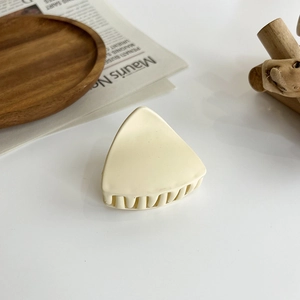 Detail view of a matte cream triangular hair claw clip on a rustic wooden plate