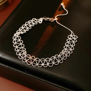 Detail of silver lace cutout woven bracelet on textured black leather backdrop