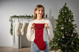 Detail of red cable-knit Christmas stocking held in a cozy festive holiday setting
