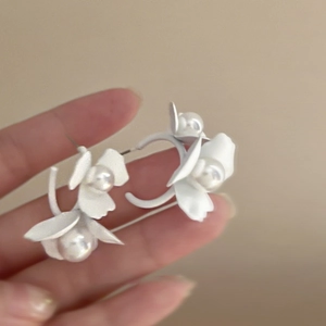 Elegant C-shaped white floral earrings with center pearl studs shown in hand close-up