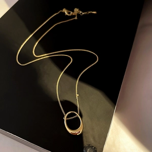 Detail view of a gold oval geometric pendant necklace on a sleek black background