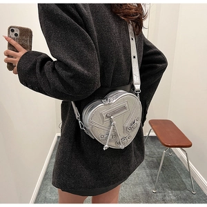 Détail du sac bandoulière argenté en forme de cœur avec rivets et pompons en cuir