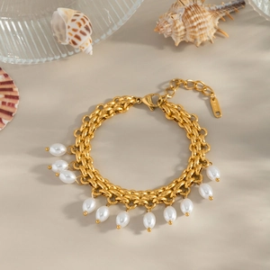 Détail d'un bracelet tressé doré avec perles et étiquette S.Steel sur une surface beige
