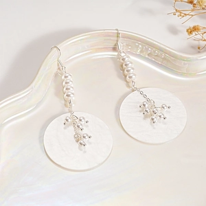 Détail de boucles d'oreilles en perles avec pendentif rond en nacre irisée et perles blanches