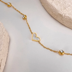 Detail of gold chain bracelet with white heart inlay and three sparkling zircon beads
