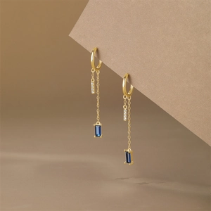 Detailed close-up of gold tassel earrings with blue rectangular gemstone and micro-zirconia