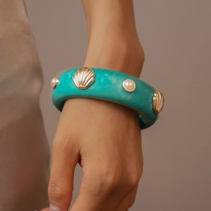 Détail du bracelet en résine marbrée verte avec breloques coquillages dorés et perles
