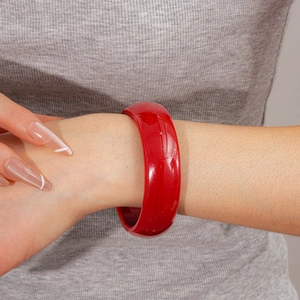 Gros plan d'un large bracelet en résine rouge poli porté sur un fond de tissu neutre