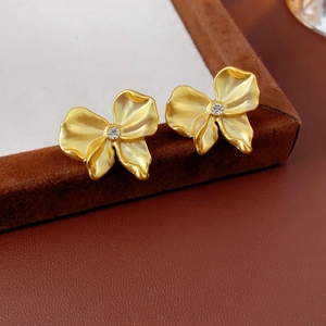 Macro view of golden bow earrings featuring folded metal petals and a sparkling center zircon