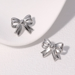 Detailed close-up of polished silver bow stud earrings on a textured background