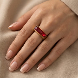 Detail of a vintage-style gold ring featuring a large rectangular red crystal on model's hand