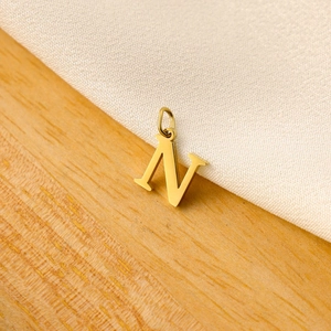 Macro shot of gold letter N pendant with loop on wooden background for DIY jewelry