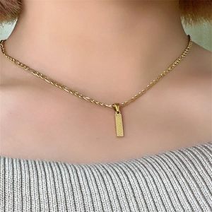 Dettaglio di una collana a catena Figaro in oro con un ciondolo a barra rettangolare testurizzato