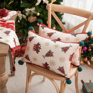 Close-up of woven Christmas pillows with festive trees and green pom-poms on a chair