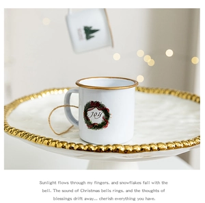 Close-up of a white enamel Christmas mug with JOY wreath on a ceramic tray with warm lights
