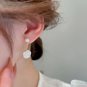 Close-up of model wearing white rose petal and pearl drop earrings with gold finish