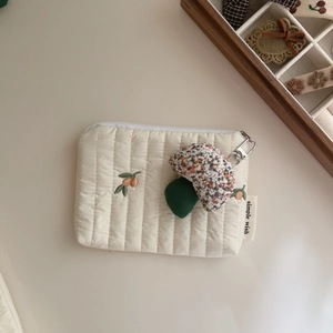 Detail of quilted off-white pouch featuring fruit embroidery and mushroom charm