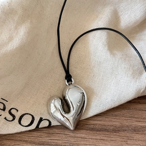 Macro detail of silver fluid heart pendant on black cord over rustic canvas