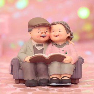 Close-up of elderly couple figurines sitting on a sofa reading, warm resin ornament detail