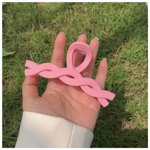Close-up of a matte pink twisted wave hair claw clip held by a hand on a grass background