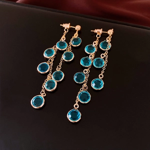 Detail view of French style gold tassel earrings with teardrop blue gemstones