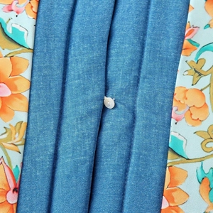 Detailansicht der blauen plissierten Jeansjacke mit floralem Print und einem Perlmuttknopf
