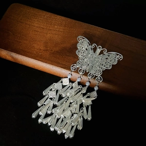 Detail of silver butterfly tassel hair clip with white pearls on a dark wood stand
