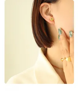 Close-up of gold-plated screw stud earrings and wing ring on model in soft lighting