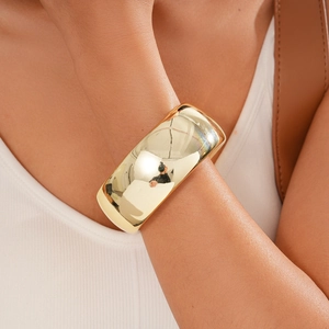 Close-up of a wide minimalist polished gold-tone metal open cuff bracelet on a model wrist
