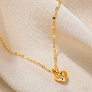 Macro shot of 18k gold heart pendant on wave chain over cream silk fabric texture