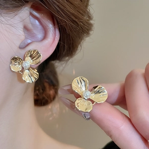 Detailed close-up of a gold metal flower stud earring with a central white pearl