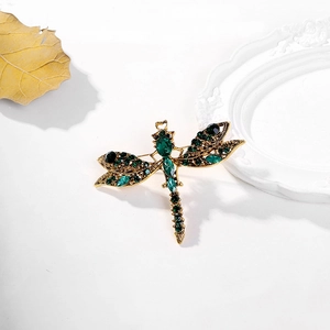 Close-up of vintage dragonfly brooch with emerald green crystals on artistic props