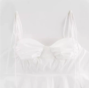 Detail of adjustable tie straps and pleated chest design on a white crop top camisole