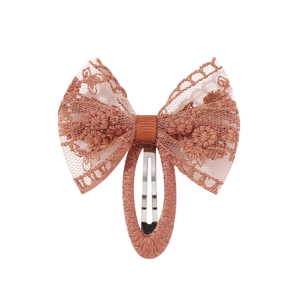 Détail du nœud en dentelle terre cuite avec broderie florale délicate sur la barrette