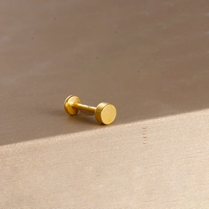 Close-up of matte gold heart-leaf stainless steel labret piercing jewelry on textured surface