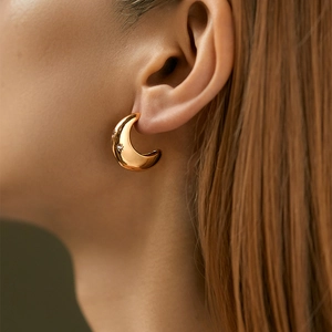 Close-up of golden crescent earrings with small rhinestones on a female model