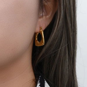 Close-up of golden textured geometric earrings showing detailed twisted metal patterns