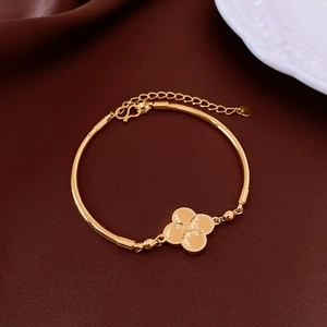 Dettaglio di un bracciale con ciondolo a quadrifoglio dorato su sfondo di seta marrone