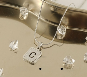 Close-up of stainless steel necklace with C pendant showing sandblasted and polished textures