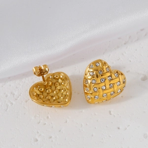 Detail of gold heart earrings with woven texture and sparkling crystals on white silk
