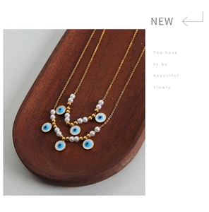 Detail of gold evil eye pendant necklace with white pearls on a rustic wooden tray