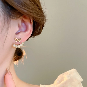 Detail view of gold bow earrings with white pearl arc worn on a model's earlobe