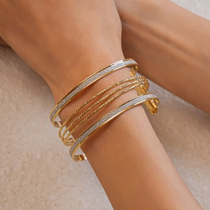 Detail of layered gold and silver textured bangle set worn on wrist with soft lighting