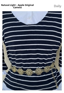 Detail of a vintage golden hollow floral metal waist chain on a striped knit garment