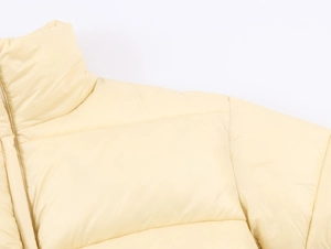 Detail of the high collar and shoulder stitching on a light yellow padded winter coat